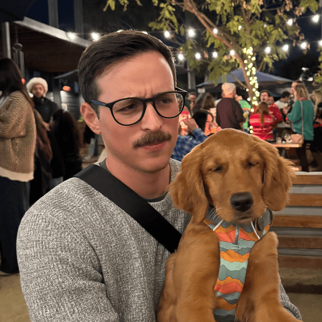 Eshed sitting outdoors with a golden retriever puppy on his lap